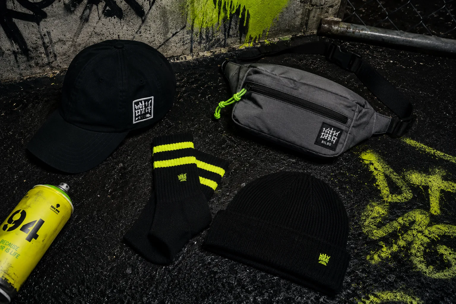 Gorras, bandolera y calcetines con detalle en verde acido sobre asfalto