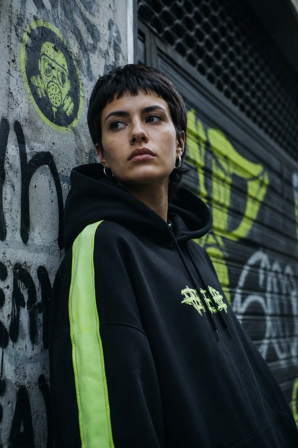 Modelo joven con sudadera oversize HZRD apoyada en pared con grafiti